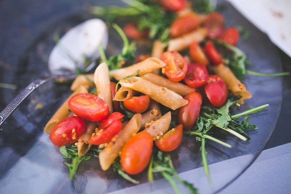 Uma salada de macarrão com tomates, azeitonas e espinafre.